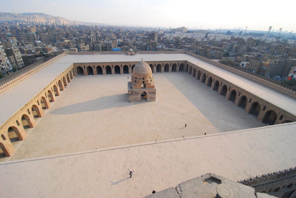 Pátio da mesquita de Ibn Tulun cercado por galerias, com edifícios do Cairo ao fundo ilustrando artigo Cairo histórico: como diferentes núcleos formaram a cidade?