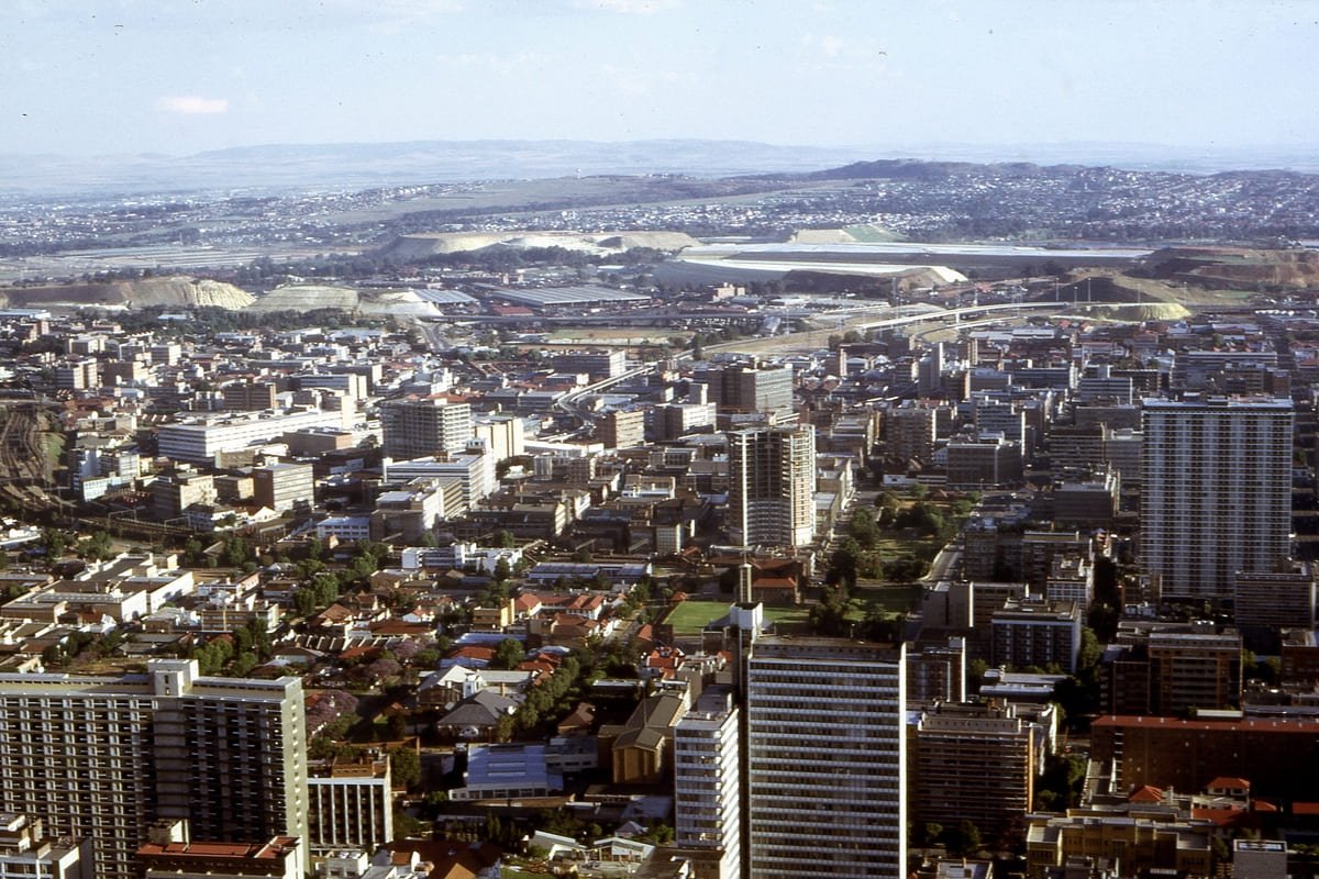 Edifícios de Joanesburgo diante de grandes depósitos claros de rejeitos de mineração em 1972, ilustrando artigo Mineração em Joanesburgo: como o ouro dividiu a cidade?