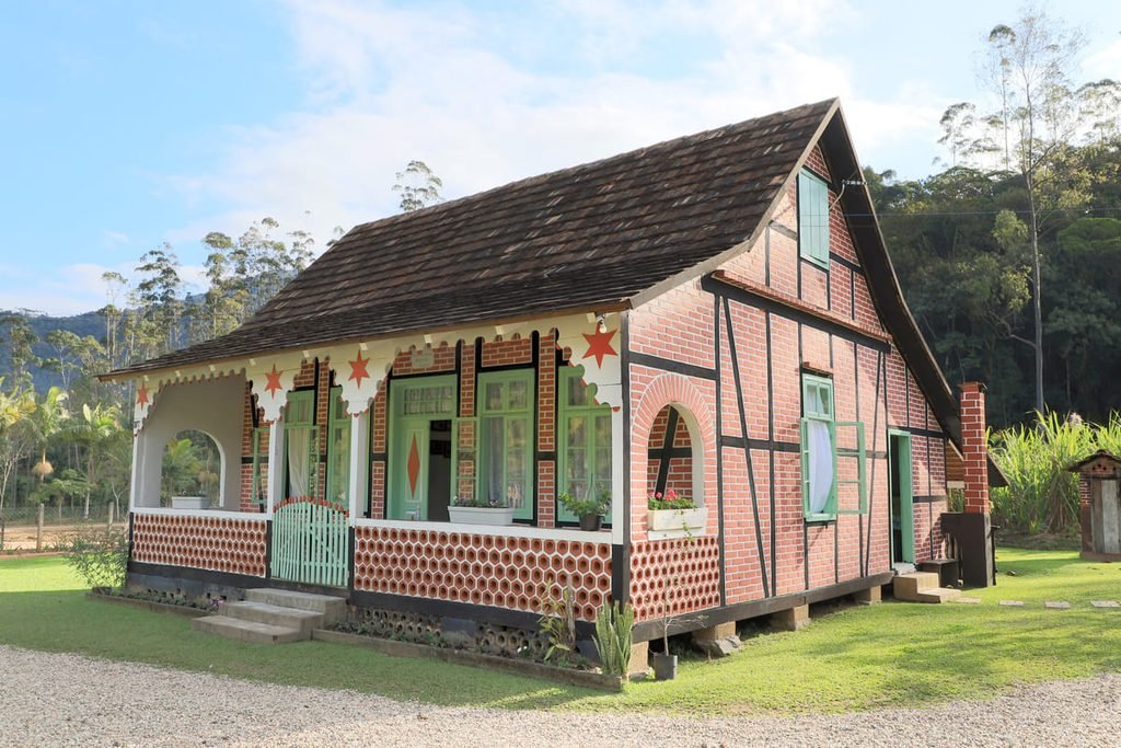 Casa Radünz, com estrutura de madeira aparente, paredes de tijolos e jardim diante da fachada, ilustrando artigo Paisagem rural de Pomerode: o que se preserva além das casas?