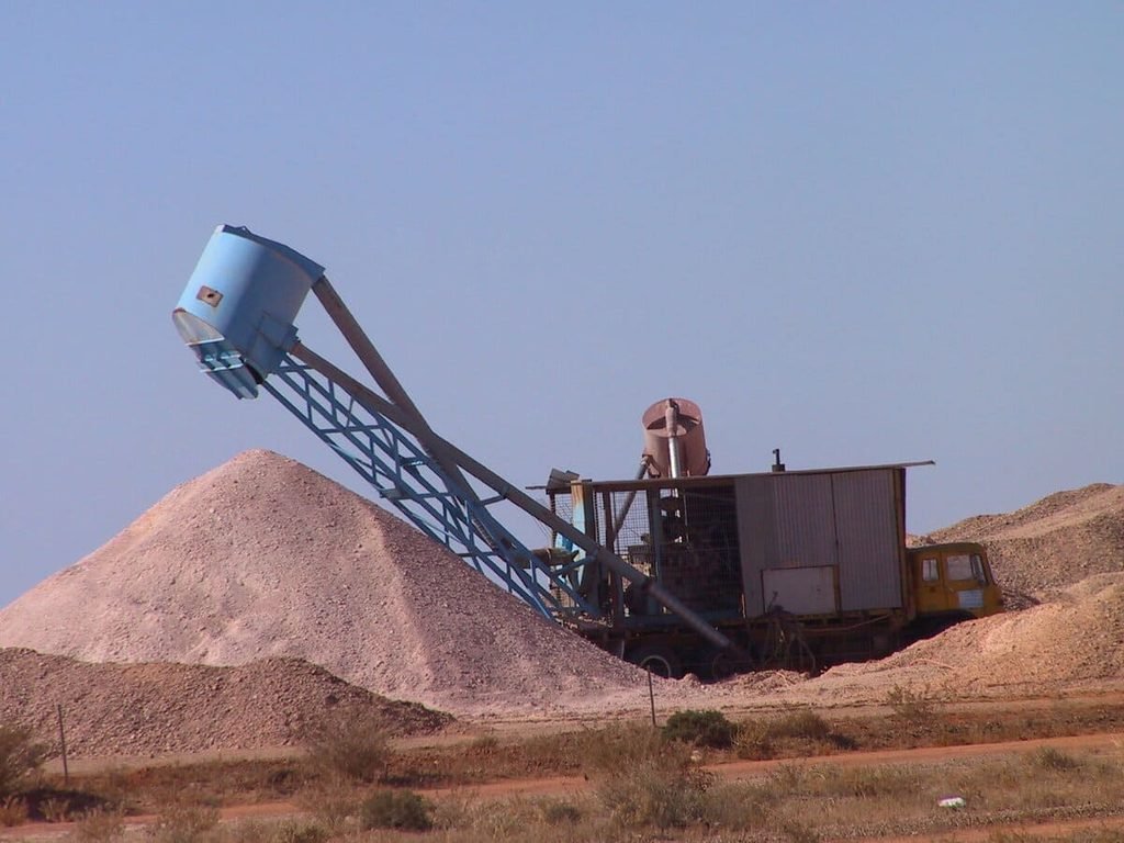 Equipamento de mineração com tubulação junto a montes de material escavado em Coober Pedy., ilustrando artigo Mineração em Coober Pedy: como a opala moldou a cidade?