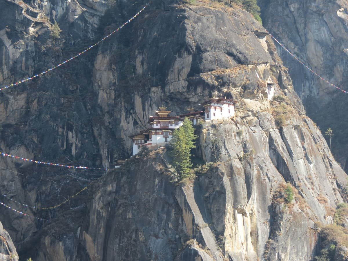 Mosteiro de Taktsang junto a um penhasco, cercado por parede rochosa e encostas vegetadas. Ilustrando artigo Lugares sagrados do Himalaia: como organizam a paisagem?