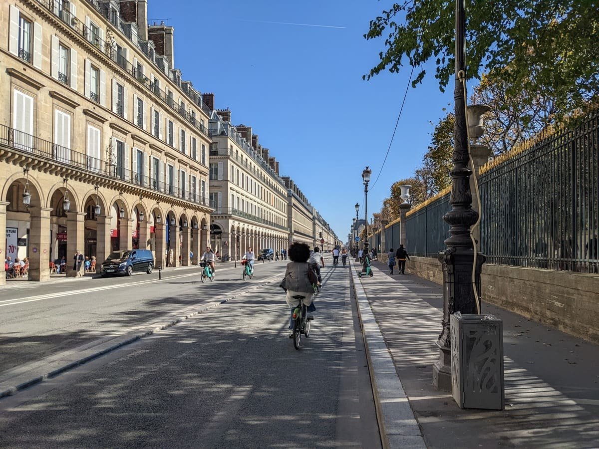 Pessoas caminhando e descansando junto ao Sena, com uma bicicleta e uma ponte ao fundo. Ilustrando artigo Paris de bicicleta: como as ruas estão mudando?