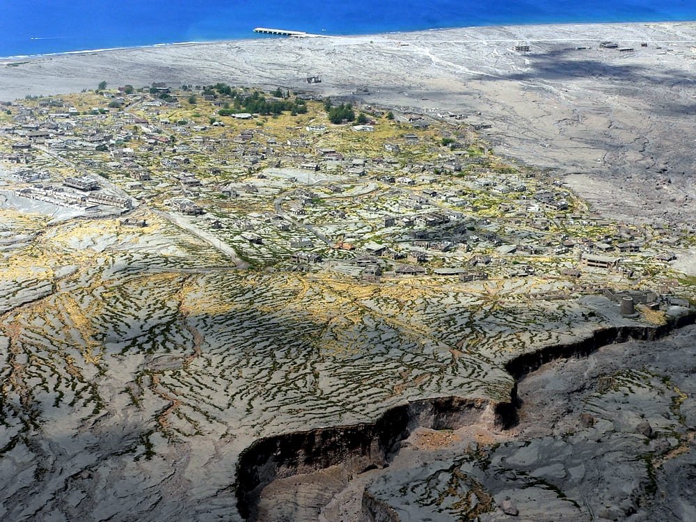 Vista aérea de Plymouth com construções remanescentes entre depósitos vulcânicos junto ao litoral. Ilustrando artigo Ilhas nas Américas: o que define seu isolamento?