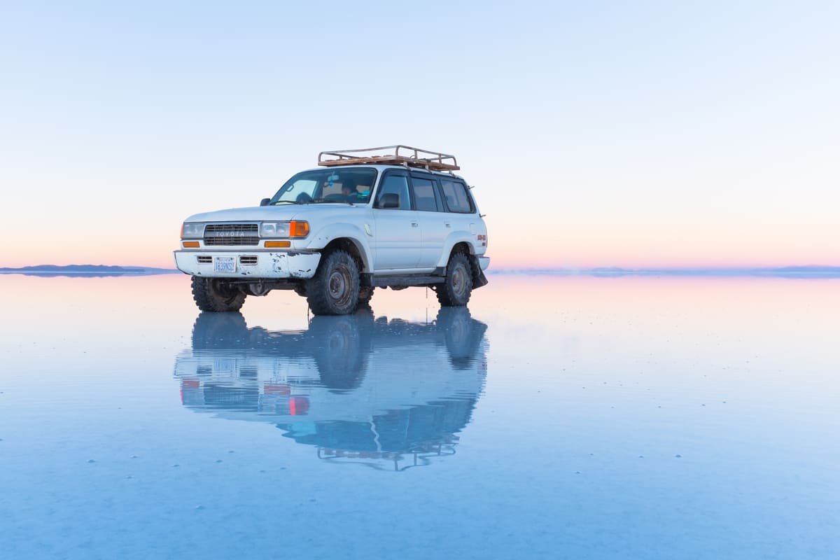 Veículo e céu refletidos na água sobre um trecho do Salar de Uyuni. Ilustrando artigo Paisagens da Bolívia: por que são tão diferentes?