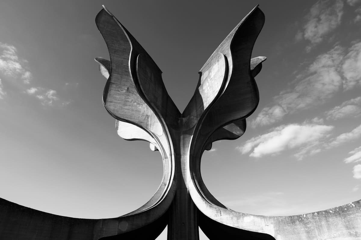 Monumento da Flor de Jasenovac visto de baixo, com superfícies curvas de concreto contra o céu, em fotografia em preto e branco. Ilustrando artigo Monumentos de concreto na Europa: por que estão ali?