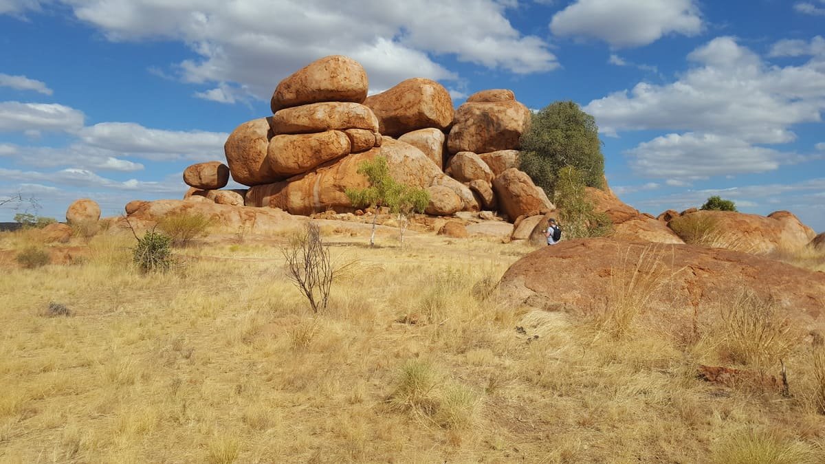 Grandes blocos arredondados de granito em Karlu Karlu, cercados por vegetação baixa e árvores. Ilustrativo ao artigo Interior australiano: como se formaram essas paisagens?