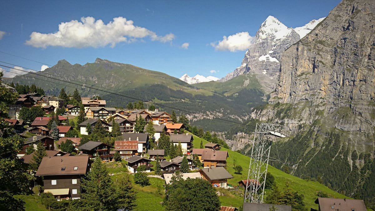 Casas de Mürren numa encosta verde, com cabos de transporte e montanhas rochosas ao fundo. Ilustrativo ao artigo Vilarejos suíços: como o relevo organiza a ocupação?
