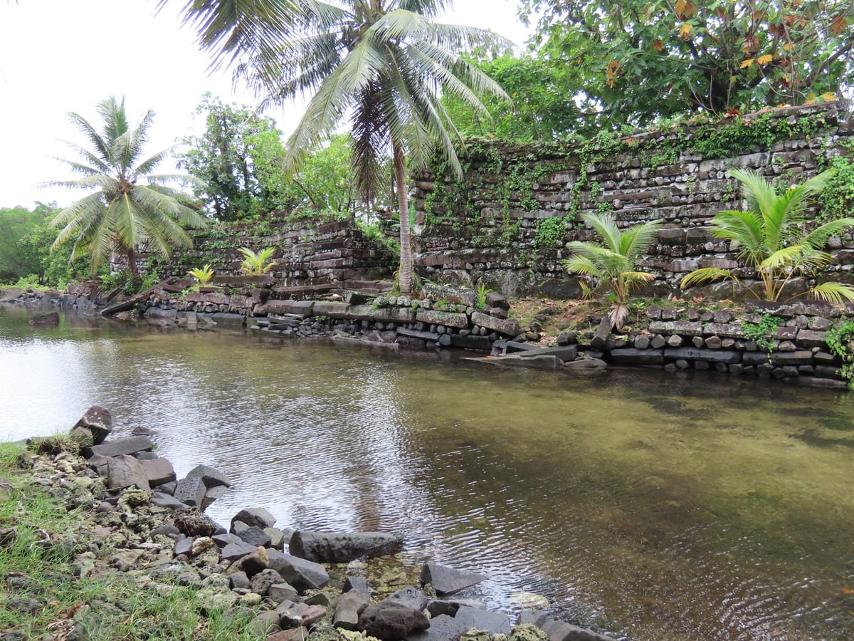 Paredes de pedra de Nan Madol junto a um canal, com vegetação sobre as estruturas e nas margens. Ilustrativo ao artigo Vestígios da Oceania: o que revelam sobre o território?