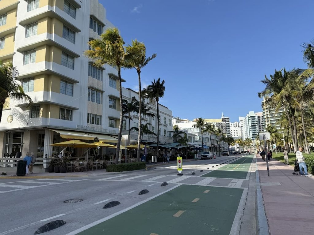 Ocean Drive em Miami Beach, com fachadas, mesas externas, palmeiras, ciclovia e pessoas na calçada. Ilustrando artigo Paisagem urbana de Miami: o que explica seus contrastes?