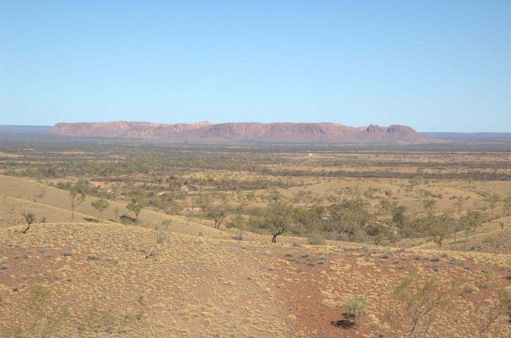 Elevações de Tnorala vistas à distância, acima de uma planície com vegetação esparsa. Ilustrativo ao artigo Interior australiano: como se formaram essas paisagens?