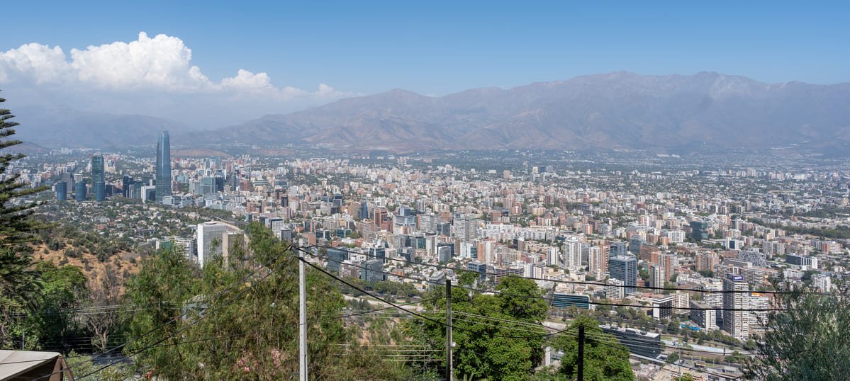 Vista elevada de Santiago, com edifícios distribuídos pela área urbana e montanhas ao fundo. Ilustrando artigo Santiago do Chile: como o relevo participa da cidade?
