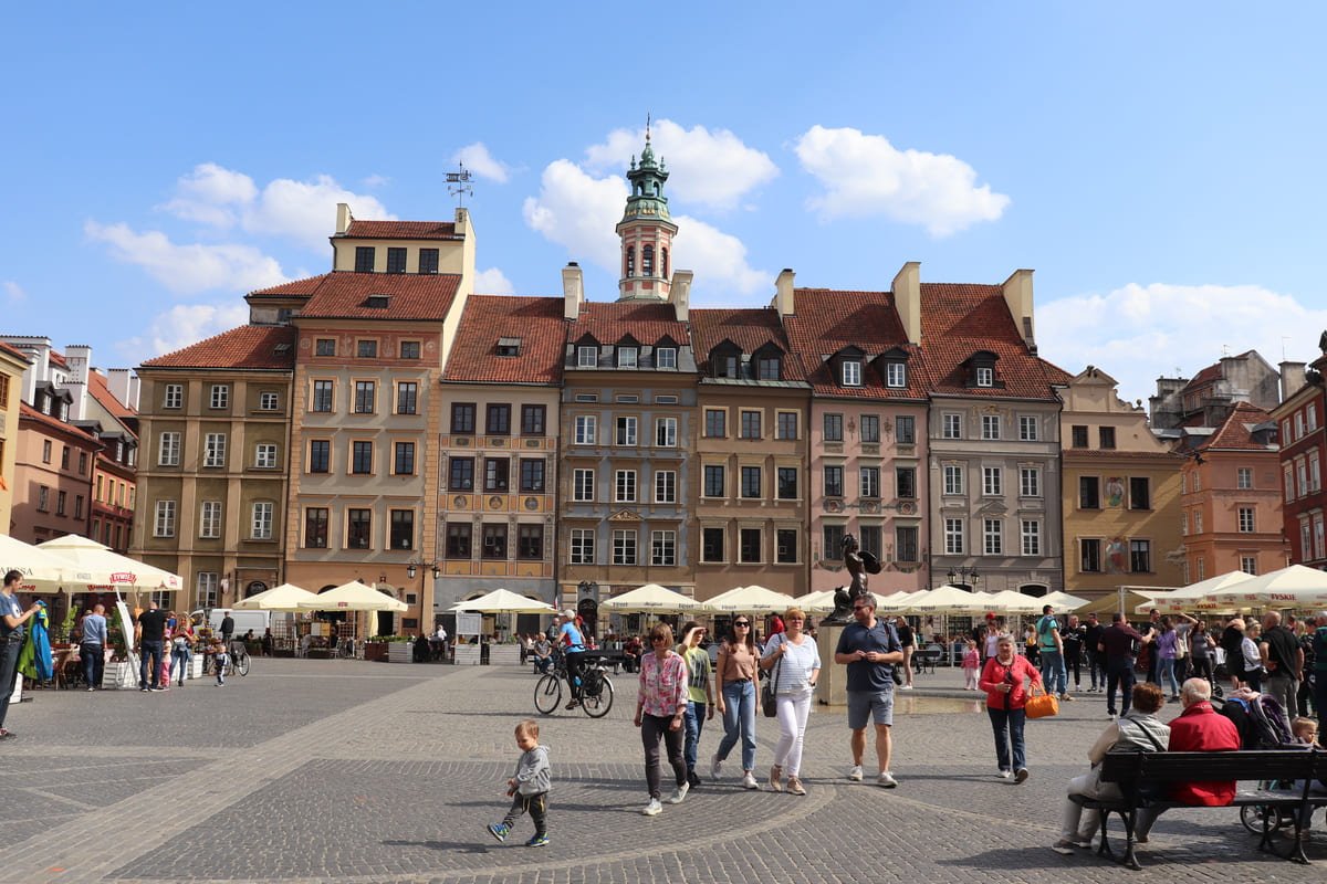 Fachadas coloridas diante da Praça do Mercado da Cidade Velha de Varsóvia, com pessoas, bancos e mesas externas. Ilustrando artigo Destinos históricos: o que observar além dos monumentos?