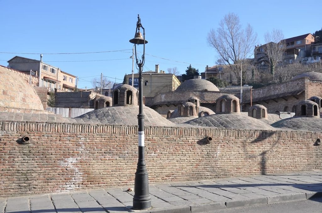 Cúpulas de tijolos dos banhos de Abanotubani diante de edifícios do bairro. Ilustrativo ao artigo Banhos de Tbilisi: por que se concentram em Abanotubani?