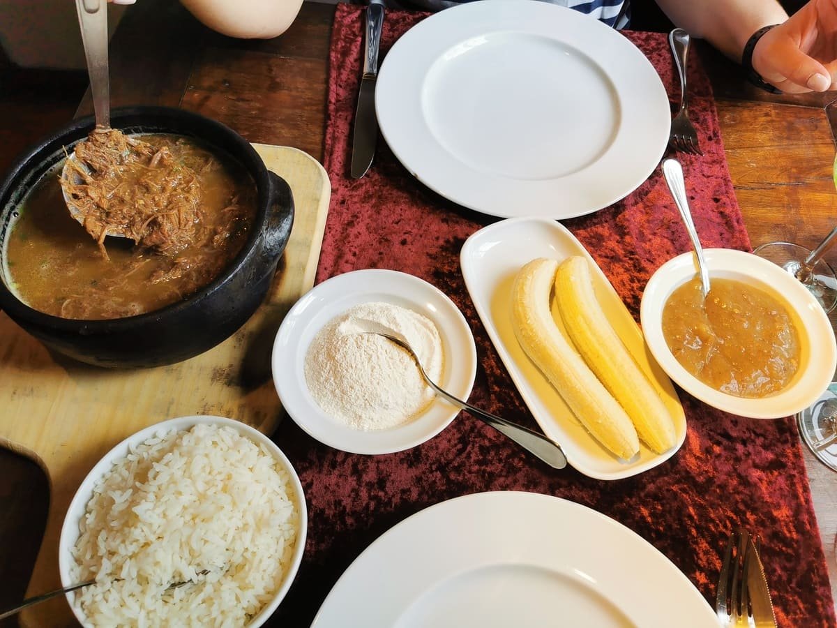 Panela com barreado sobre uma mesa, acompanhada de arroz, bananas e outros recipientes. Ilustrativo ao artigo Comida regional: o que liga um prato ao lugar?