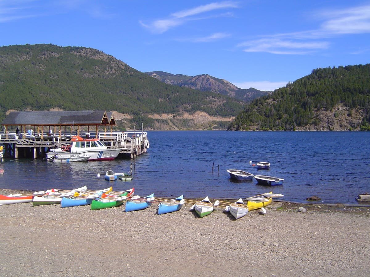 Embarcações na margem do lago Lácar, com cais e montanhas arborizadas ao fundo, em San Martín de los Andes. Ilustrativo ao artigo Além de Bariloche: o que muda entre os lagos andinos?