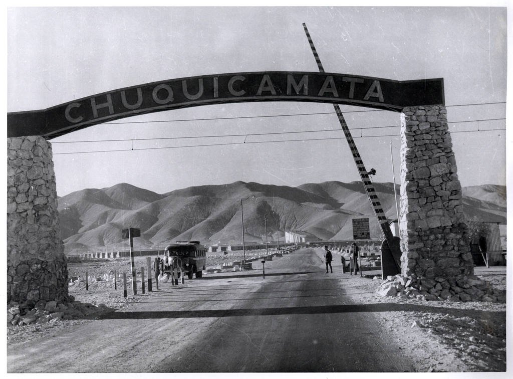 Portão de pedra e placa na entrada da mina de Chuquicamata, em fotografia em preto e branco, ilustrando artigo Lugares Mostrados em Diários de Motocicleta