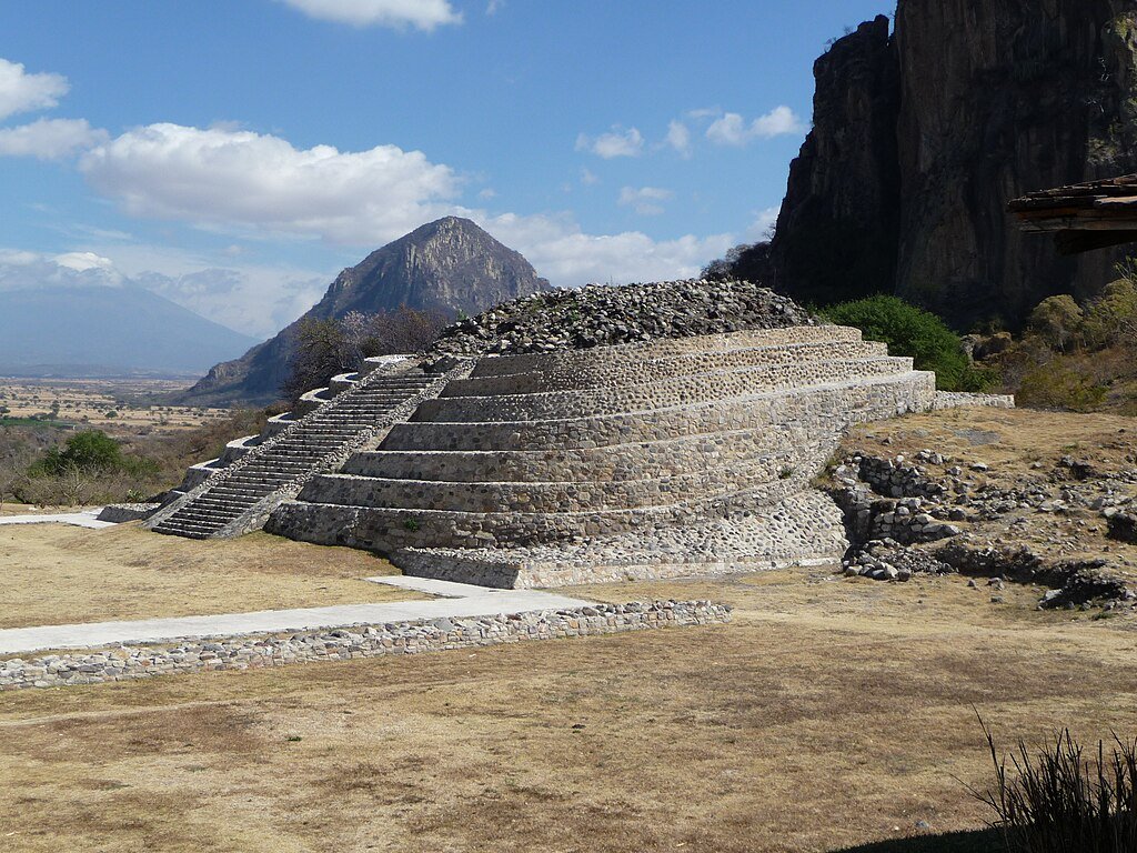 Pirâmide em Chalcatzingo, escadaria, terraços, em rochas, que ascendem ao alto. Ao lado, cerro del Mono e vulcão Popocatépetl. Estas pirâmides foram construídas pelos Olmecas, considerados uma das primeiras civilizações da Mesoamérica. É um exemplo de pirâmides pelo mundo.