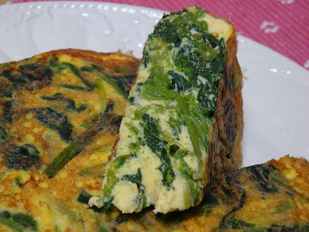 Omelete de espinafre e queijo colocados sobre prato branco e toalha rosa com desenhos brancos. Uma receita de café da manhã para dieta cetogênica.